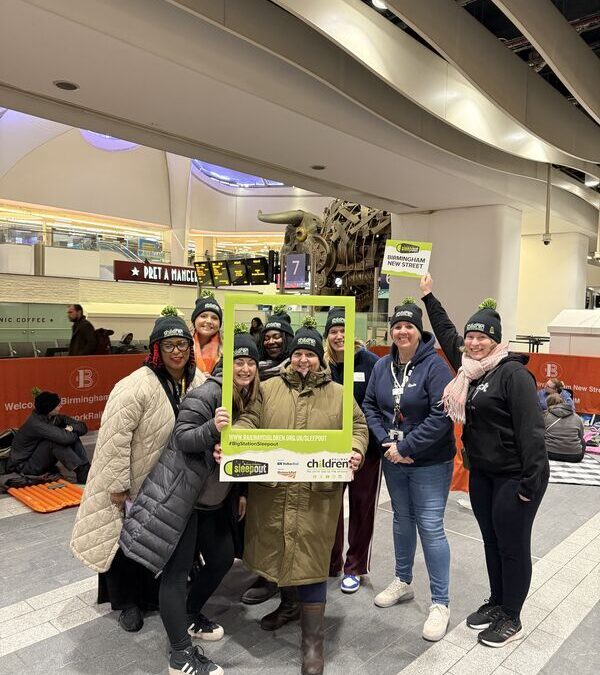 Group of people stood with a green selfie frame in Birmingham New Street station.