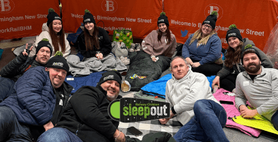 Group of people lay on the floor with sleeping bags. Logo says: Sleepout.