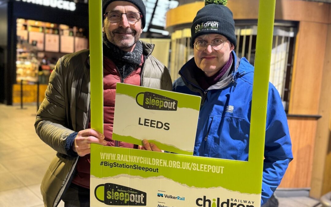 Two men dressed in winter clothing holding a selfie frame.