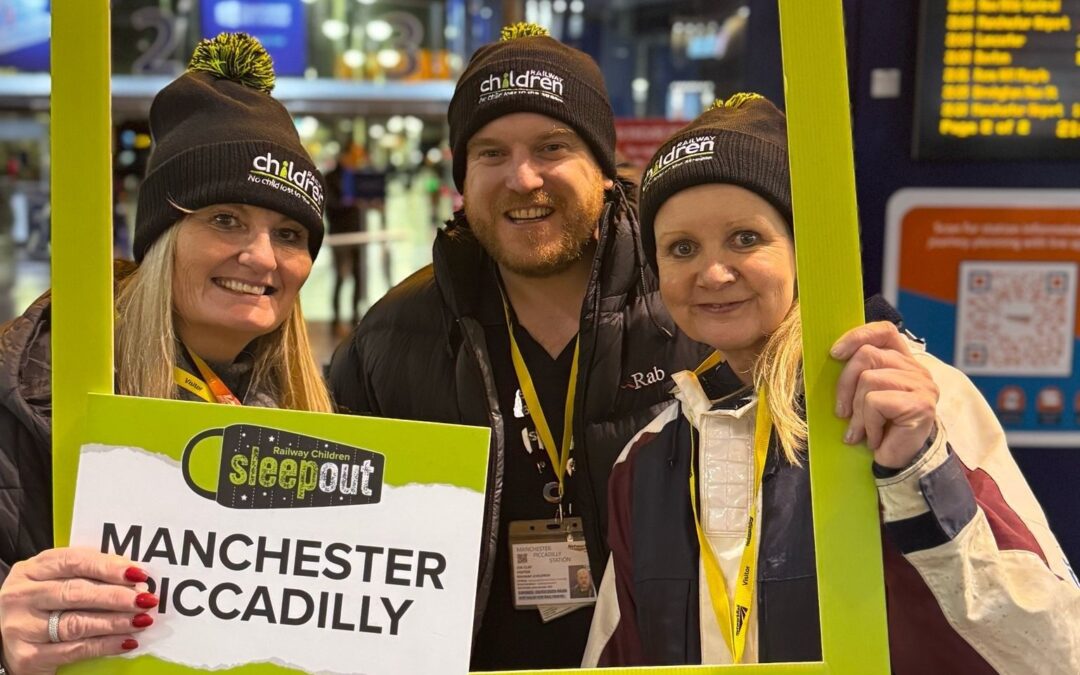 A man and two women stood holding a selfie frame and sign. Text reads: Manchester Piccadilly.