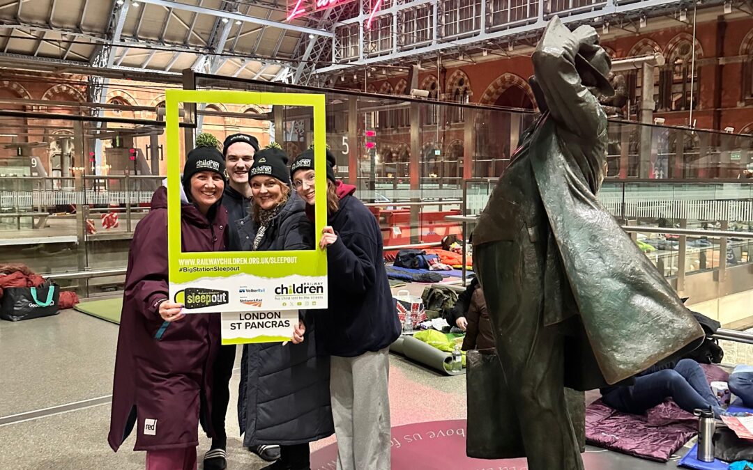 Group of people stood holding a green selfie frame in a train station.