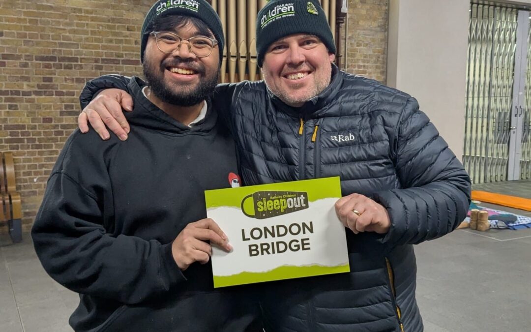 Two men dressed in dark clothing holding a sign. Text reads: London Bridge.
