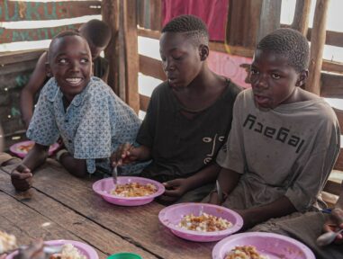 Three boys sat at a table eating food together.