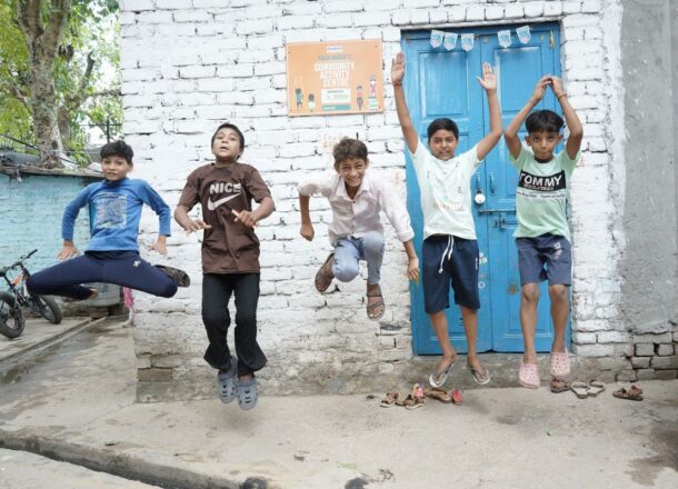 A group of boys in front of a Railway Children India child activity centre jumping in the air.