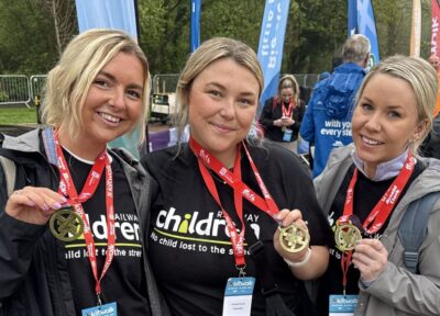 Three women taking part in an event with medals round their necks and wearing Railway Children T-shirts.