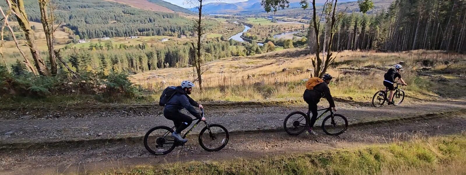 Three cyclists on a dirt track. Forest scenery in the background.