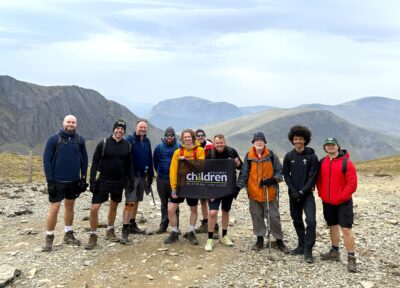 A group of people posing with a Railway Children flag in Snowdonia National Park.