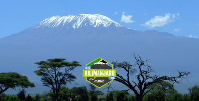 Image of a tall snowy mountain, blue skies with trees in front. Logo reads: 2025 Kilmanjaro Trek.