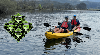 Two men wearing yellow lifejackets in a canoe on a lake with a logo next to them which reads The Scotland Triple, The Wales Triple, The England Triple and The Ireland Triple.