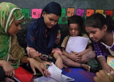 Group of girls and young boy reading through a book whilst sat on the floor.
