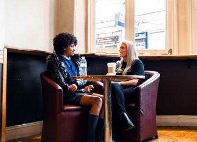 Female project worker sat with teen school girl at a coffee shop.