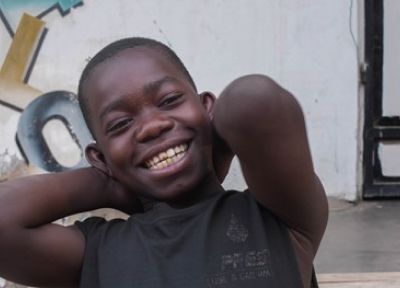 Young boy with his arms behind his head, smiling at the camera.
