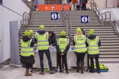 Event volunteers facing away from camera wearing yellow hi-vis jackets. They are facing a staircase.