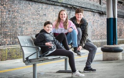 Three teenagers sitting on a railway station platform in the UK.