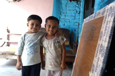 Two young boys in India stood together smiling with their arms round each other.