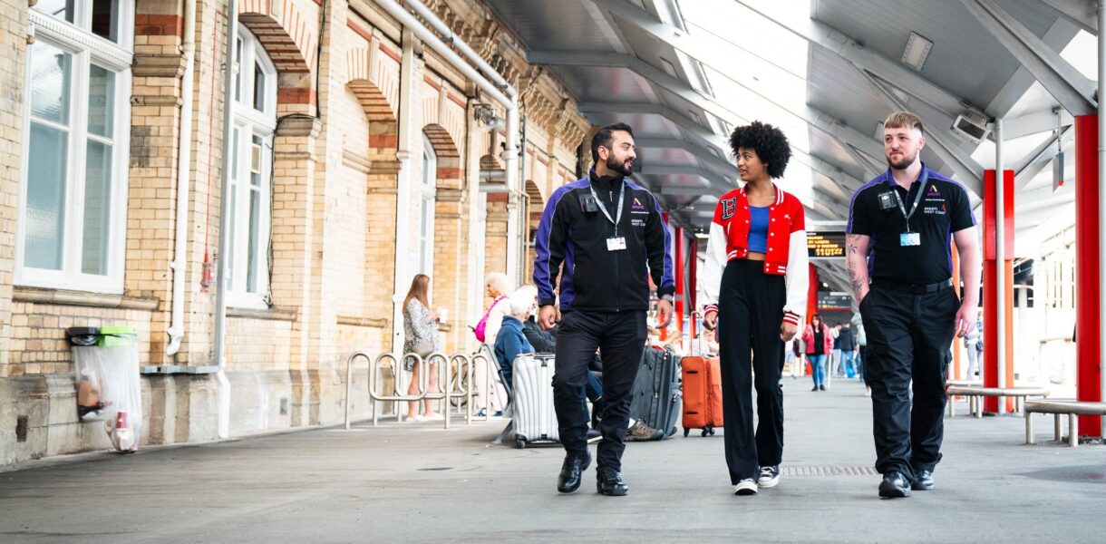 Two safeguarding officers walking with and talking to a teenage girl at a train station in the UK.