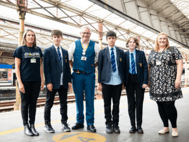 A Railway Children youth practitioner, three young teenagers, an Avanti West Coast staff member and a social worker all stood in a group on a train station platform in the UK.
