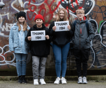 UK vulnerable children standing against graffiti wall smiling holding up thank you signs