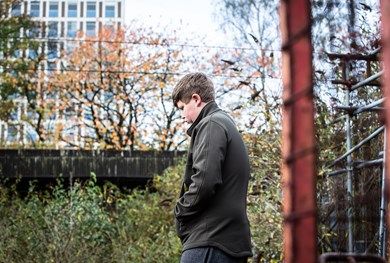Teenage boy walking with his hands in his pockets outside a train station and looking at the floor.