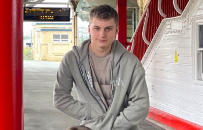 Teenage boy, hands in pockets, smiling and looking at camera.