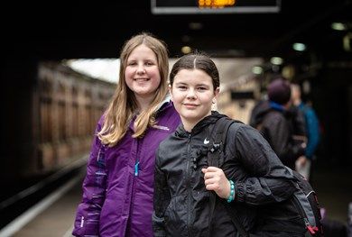 Two teenage girls smiling for camera. One is wearing a black backpack.