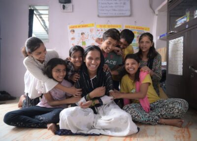 A Railway Children India project worker sat on the floor surrounded by children all looking happy.
