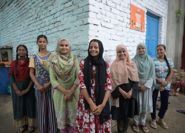 Indian girls posing for camera in front of white brick wall.