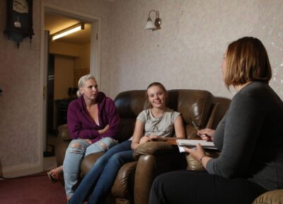 female child sitting on sofa with parent and youth practitioner.