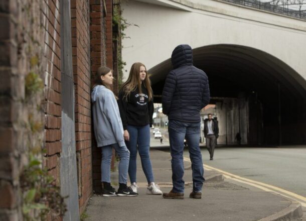children in street speaking to hooded older teenager