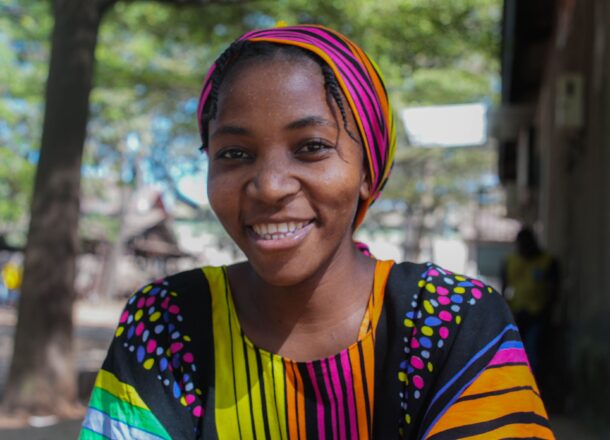 An older teenage girl in Tanzania smiling at the camera and wearing colourful clothing.