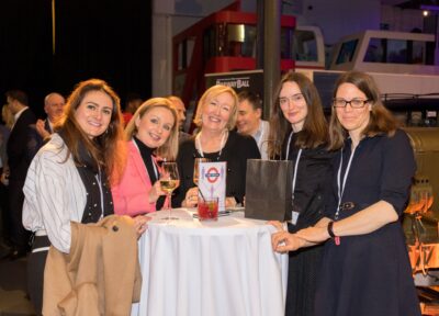 Five women stood with drinks at a function.