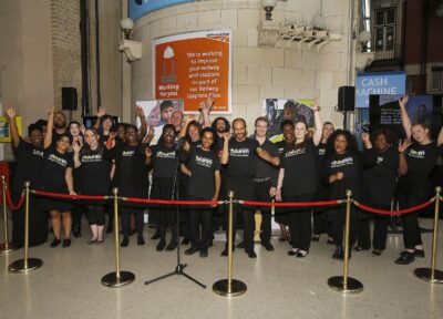 Mixed group of people stood cheering in a train station.