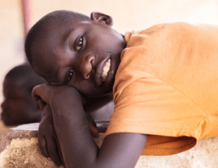Boy lying down and leaning his head on his arms, smiling at the camera.