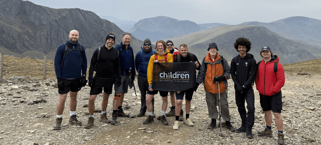A group of people stood on the top of Snowdon holding a Railway Children flag.