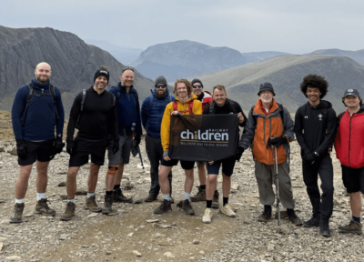 A group of people stood on the top of Snowdon holding a Railway Children flag.