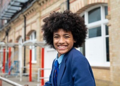 Young girl in a school uniform smiling at a train station.
