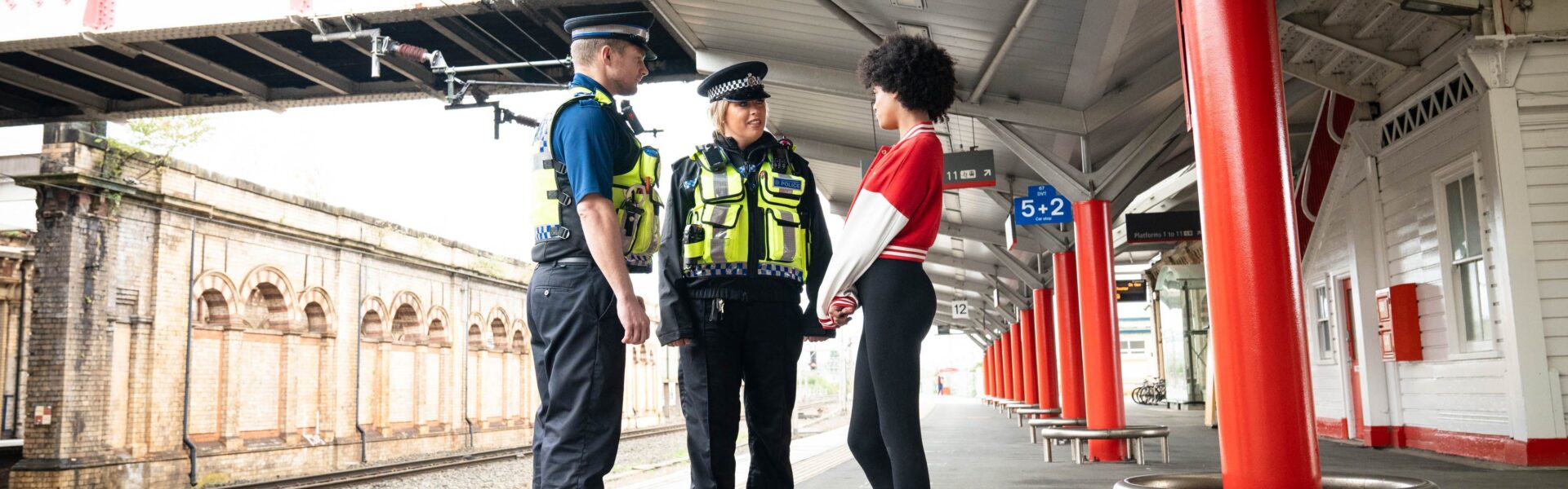British transport police officers speaking to young person on train platform.