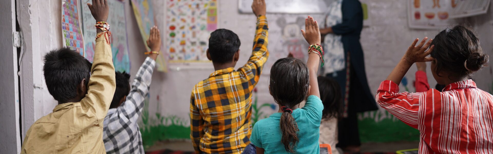 An image of a group children sat on the floor with their hands in the air in a classroom.