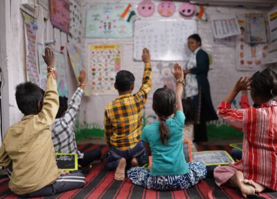 An image of a group children sat on the floor with their hands in the air in a classroom.