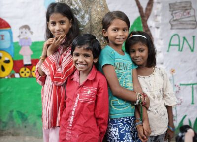 A group of children in India stood in front of a child activity centre smiling at the camera and grouped in a huddle.