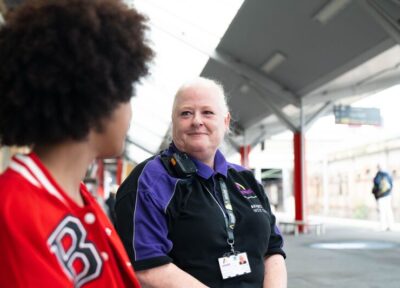 A Safeguarding Officer sat talking with a young teenage girl at a train station in the UK and smiling at her.