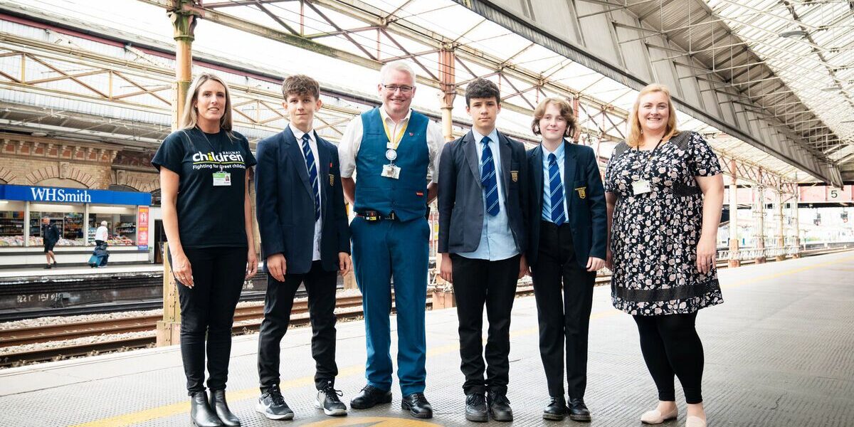 railway children workers and rail staff and young people standing on train platform