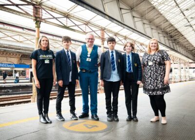railway children workers and rail staff and young people standing on train platform