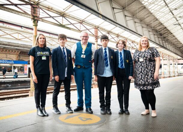 railway children workers and rail staff and young people standing on train platform