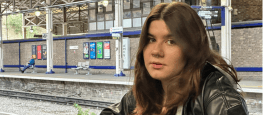 Teenage girl with brown hair and piercings leaning on a fence by a train station platform in Huddersfield.