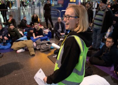 A woman in hi-vis stood in front of a group of participants at the Railway Children Sleepout in Manchester.
