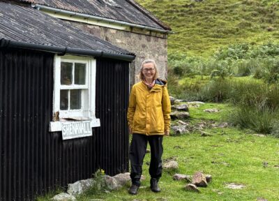 Woman in a yellow jacket stood by a black outbuilding
