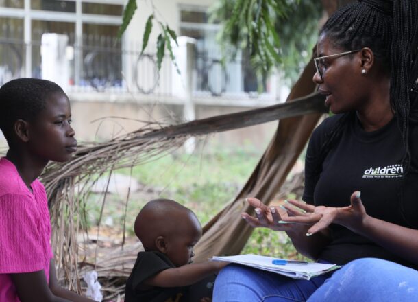 A young woman with her child sat talking to a Railway Children Africa project worker at a Youth Association.