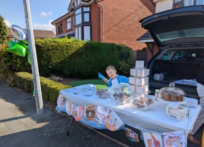 Young boy sat at a table selling cupcakes.