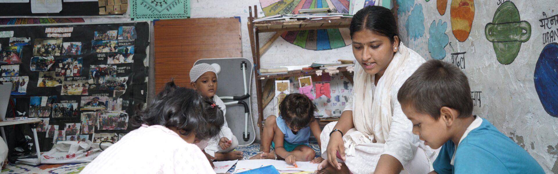 A group of children writing and drawing in a classroom in India sat on the floor with their teacher.
